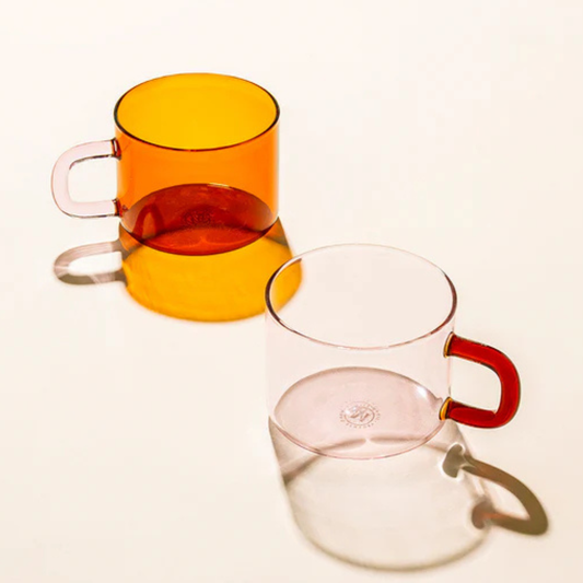 Two transparent glass mugs with colored handles on a white background