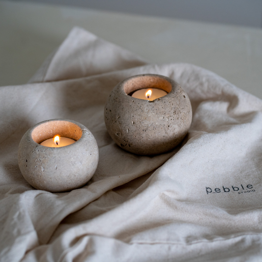 Two travertine candle holders with lit candles on a beige fabric surface.