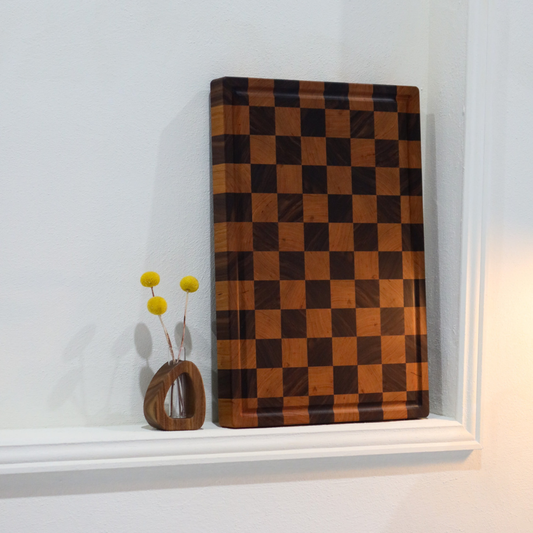 Checkered wooden chopping board on a white surface with a small decorative vase.