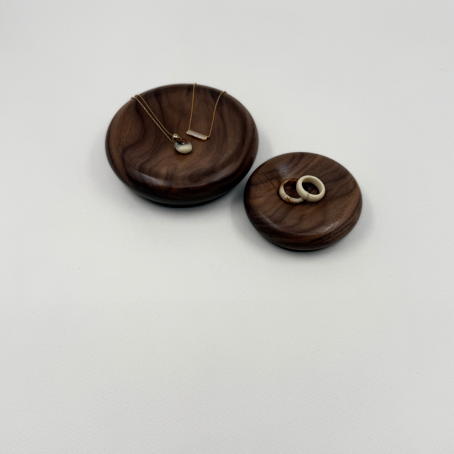 Two wooden jewellery holders with necklaces and rings on a light grey background