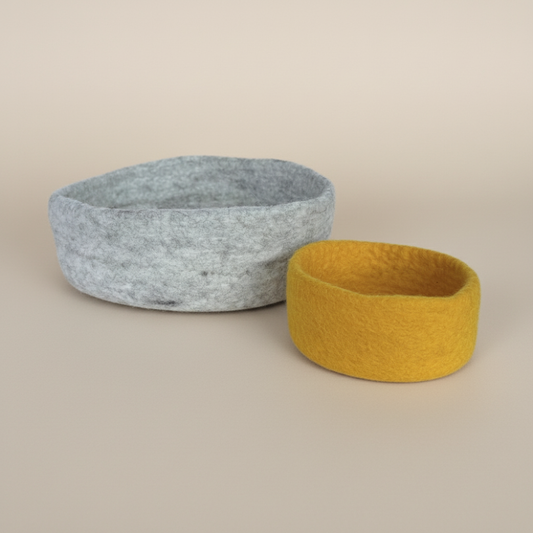 Handmade wool felt nesting bowls- one medium bowl in marbled beige and one small bowl in sunflower yellow, displayed on light background
