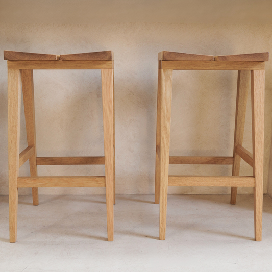 Two wooden bar stools against a plain wall.
