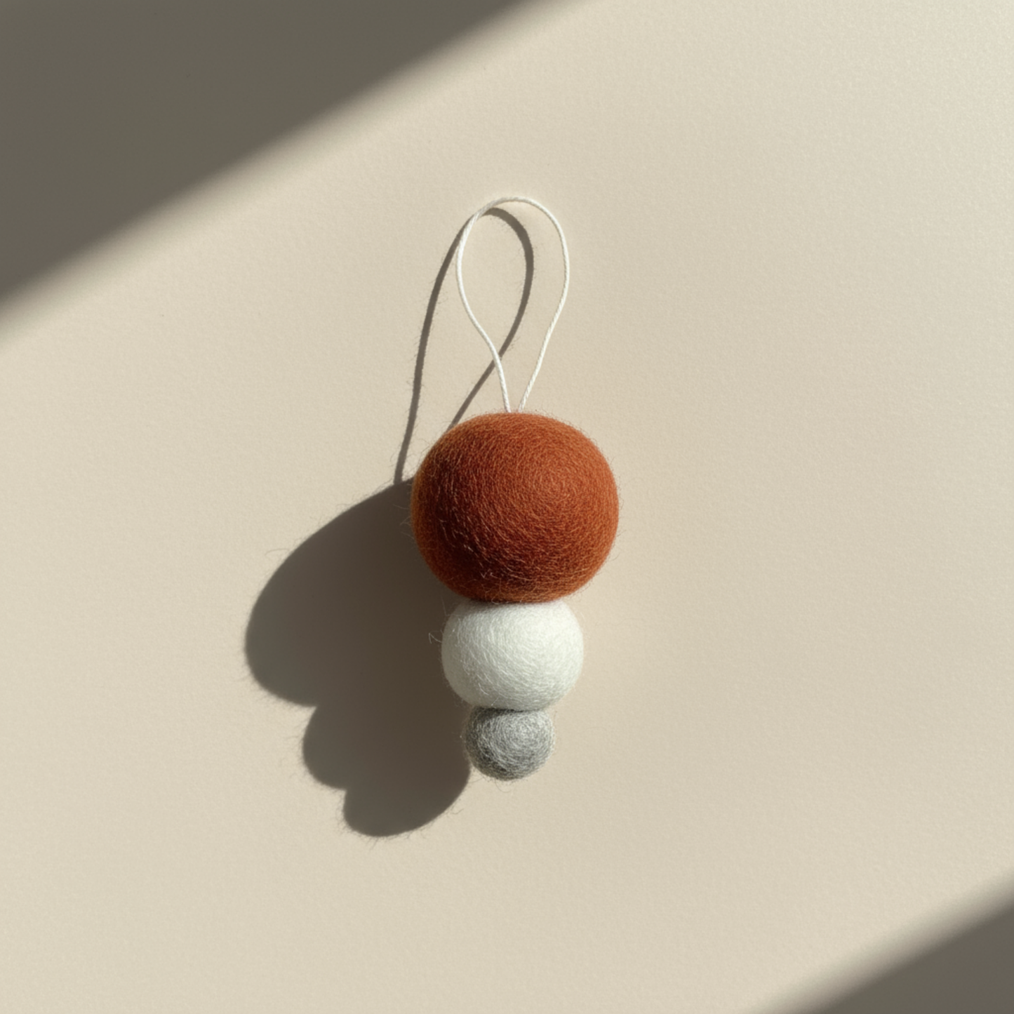 Pebble Studio Nordic Bauble in rust: three stacked felt spheres made from New Zealand wool with a hanging loop.