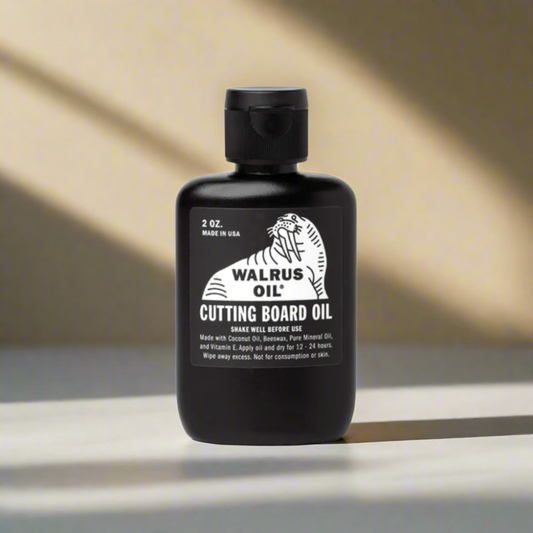 Black bottle of Walrus Oil Cutting Board Oil on a reflective surface with a neutral background
