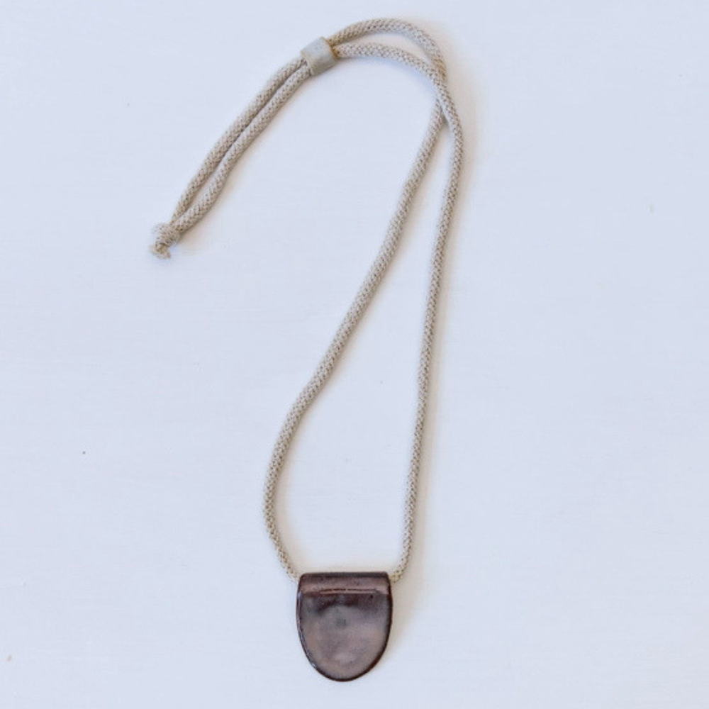 Necklace with a dark ceramic pendant on a light grey background