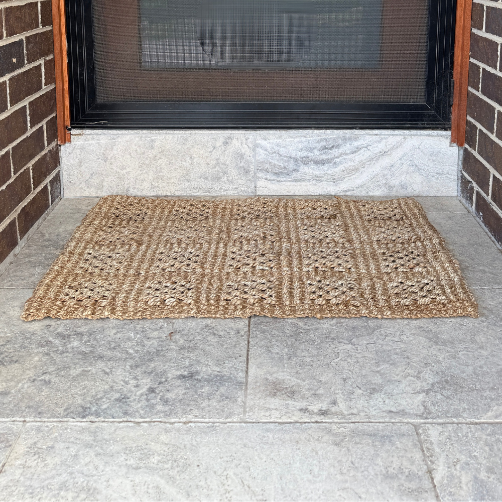 Doormat on a stone floor in front of a door with a screen