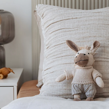 Stuffed donkey toy on a bed with a textured pillow and nightstand in the background