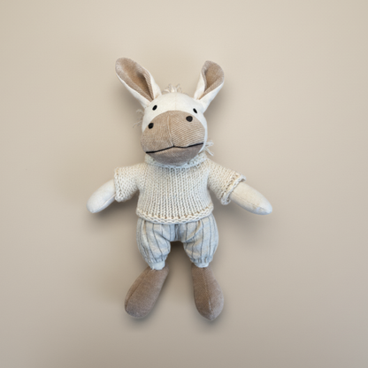 Stuffed toy donkey wearing a knitted sweater on a beige background