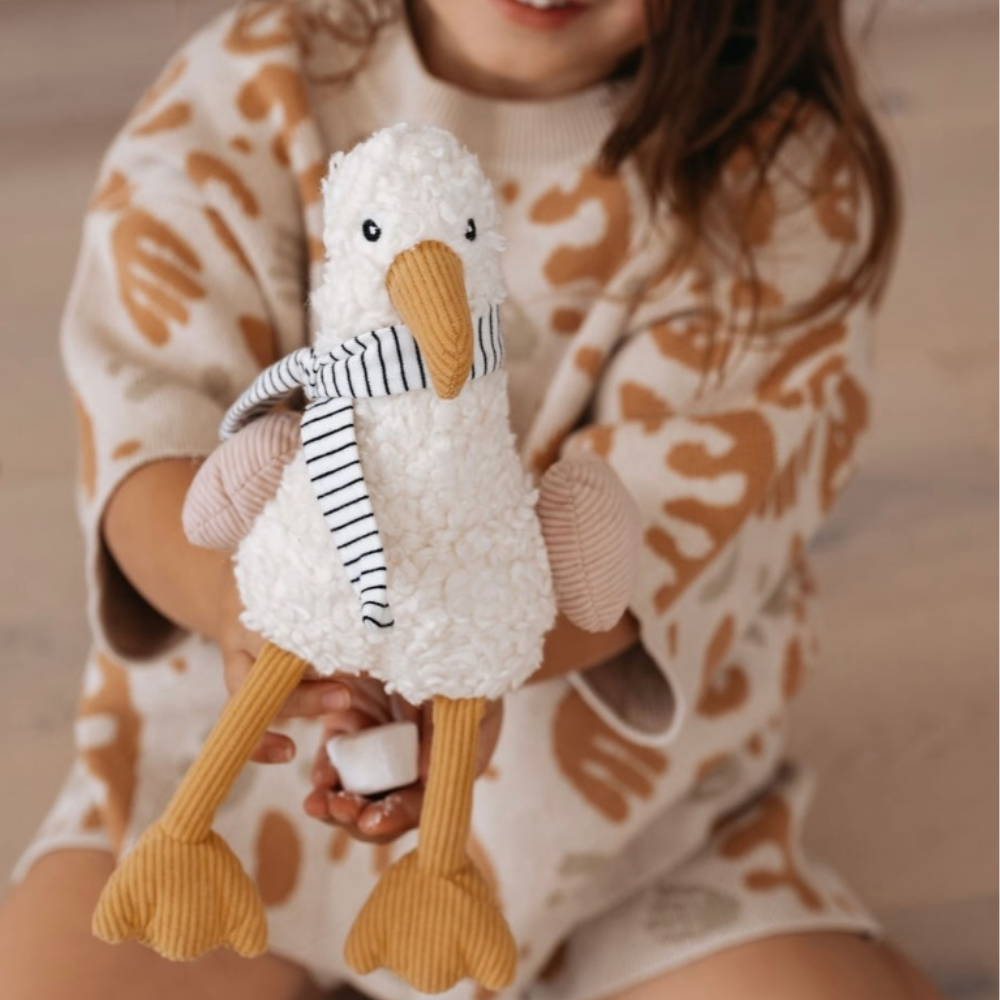 Child holding a plush toy seagull with a striped scarf
