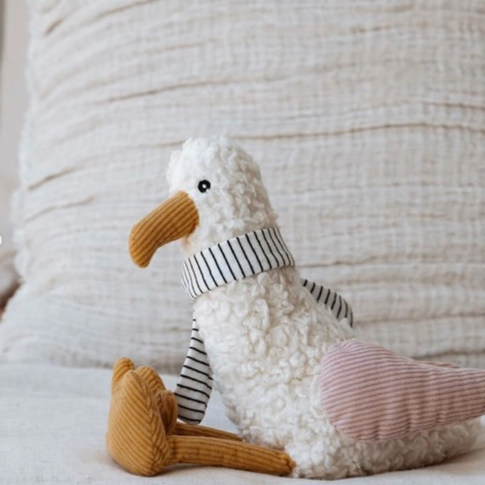 Stuffed toy seagull with a striped scarf against a textured white background