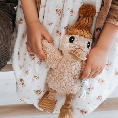 Child in a floral dress holding a knitted duck toy with a mustard hat