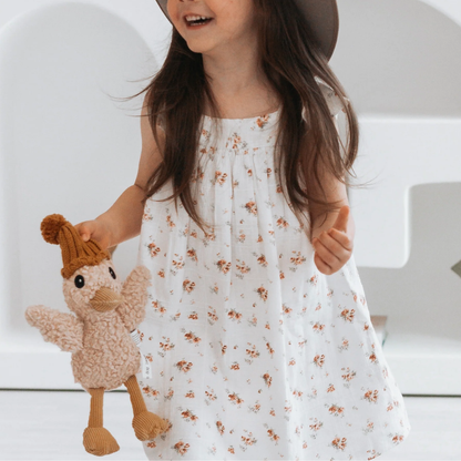 Child wearing a floral dress holding a plush toy with a hat indoors.
