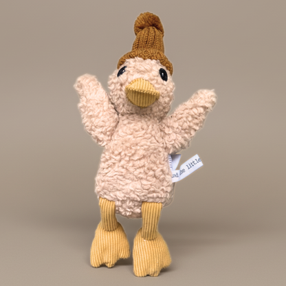 Plush duck toy with a knitted hat on a beige background