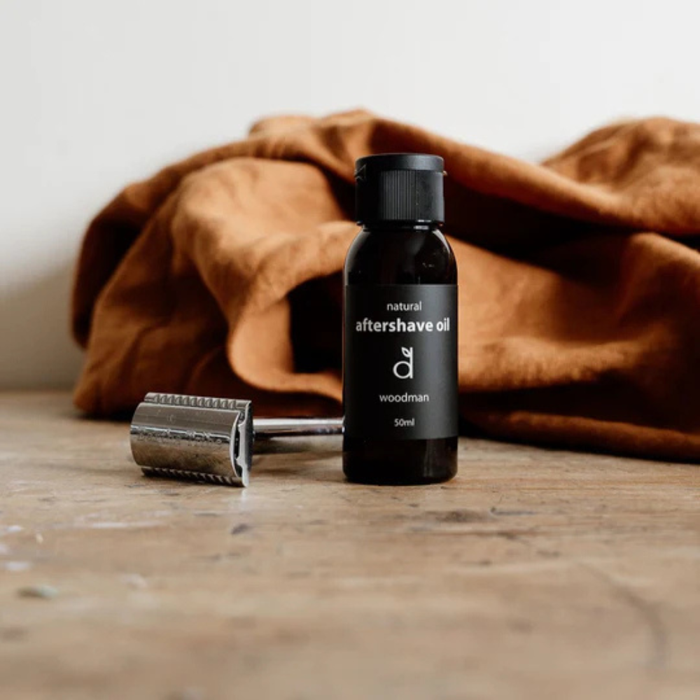 Bottle of aftershave oil with a razor and brown towel on a wooden surface