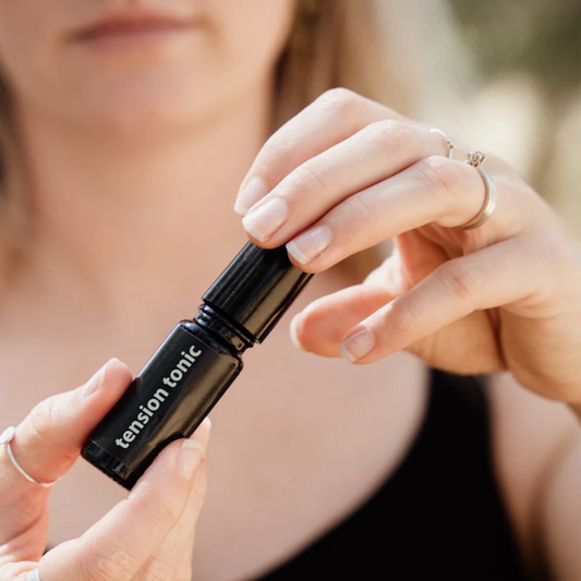 Person holding a black bottle labelled 'tension tonic' with a blurred background