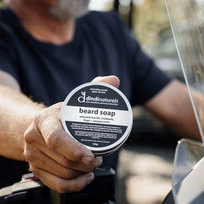 Person holding a container of dindi naturals beard soap outdoors