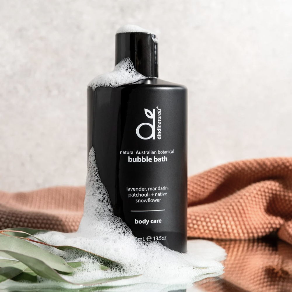 Black bottle of bubble bath with foam, surrounded by eucalyptus leaves and a towel on a light background