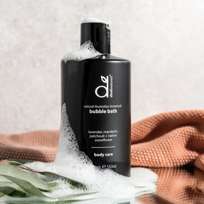 Black bottle of bubble bath with foam, surrounded by eucalyptus leaves and a towel on a light background