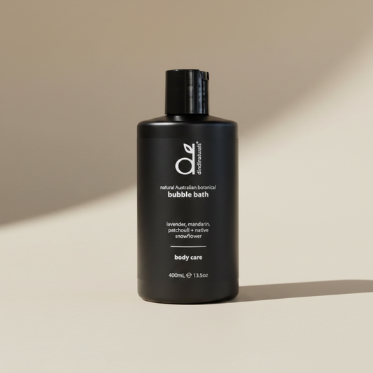 Black bottle of Dindi Naturals bubble bath with on a beige background