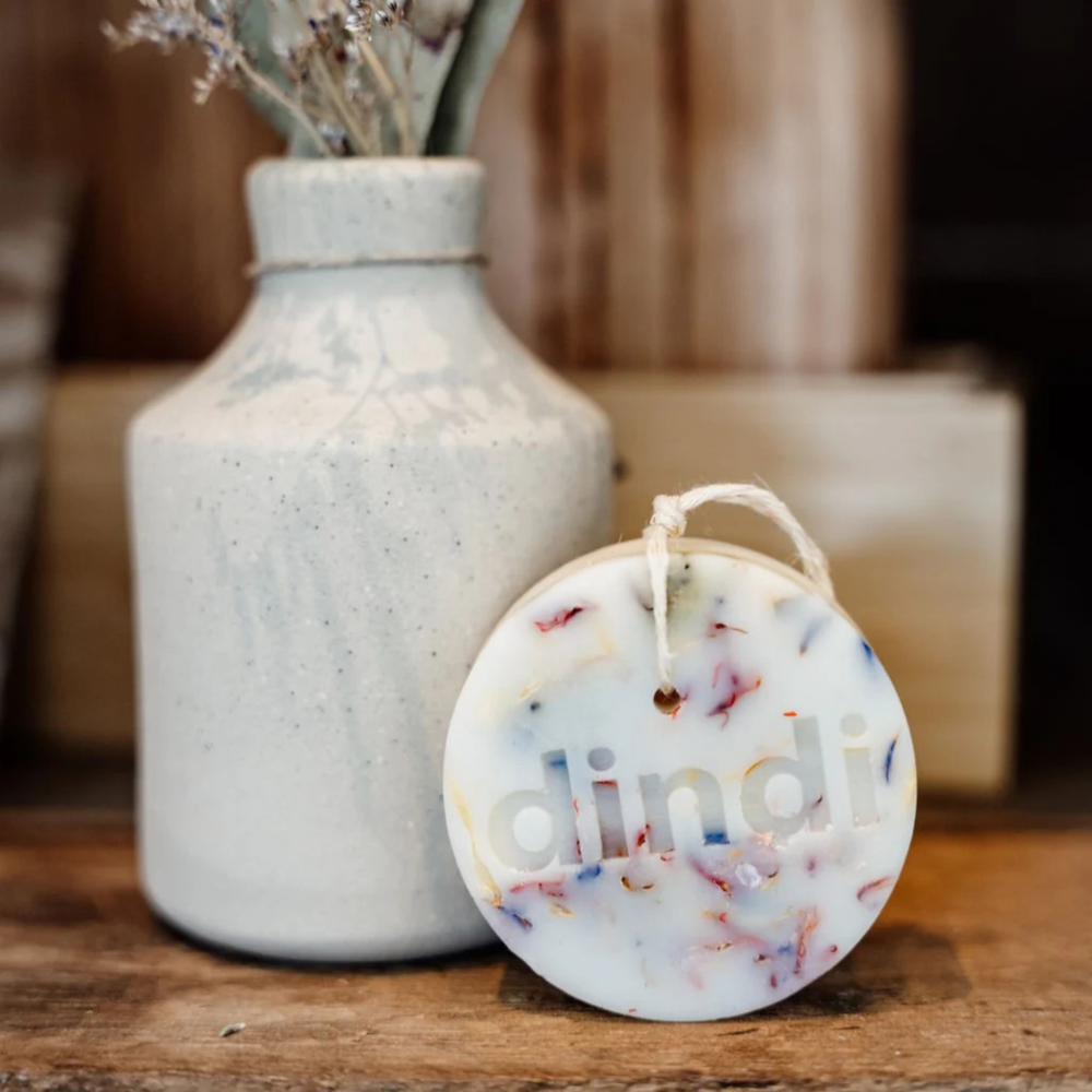 Round wax clothing protector with 'dindi' branding on the surface next to a white vase.