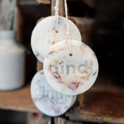 Round white was clothing protector with 'dindi' text hanging on a string against a blurred background.