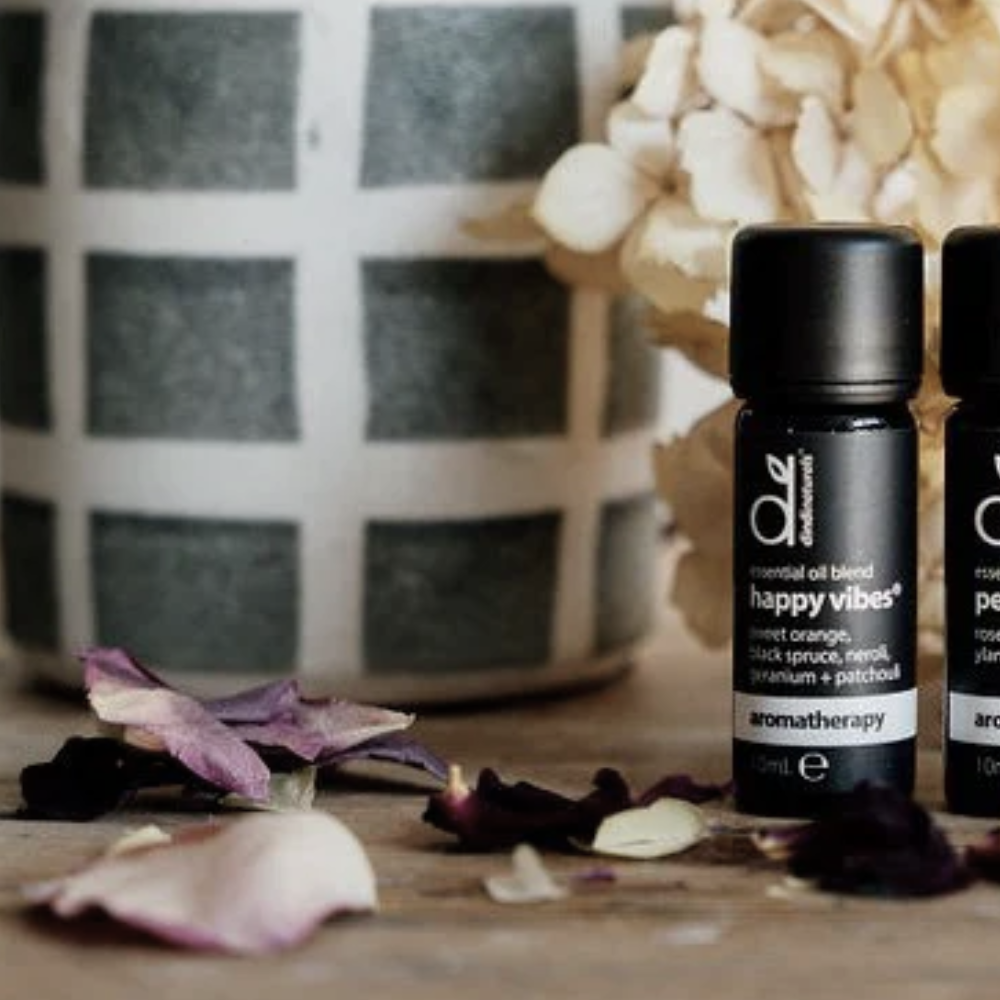 Essential Oil with 'happy vibes' label on a wooden surface with flowers and a decorative item in the background.