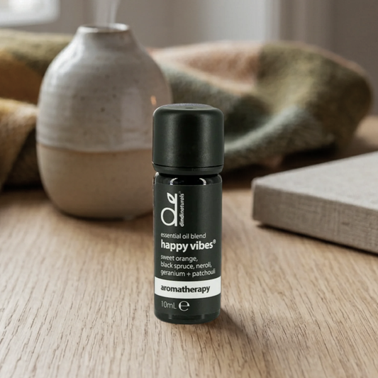 Essential oil blend bottle labelled 'happy vibes' on a wooden surface with a blurred background