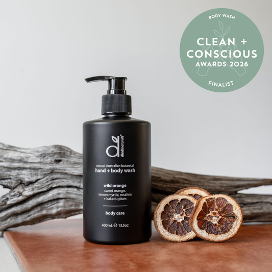 Black hand and body wash bottle with pump on a wooden surface, featuring 'Clean + Conscious' awards badge.