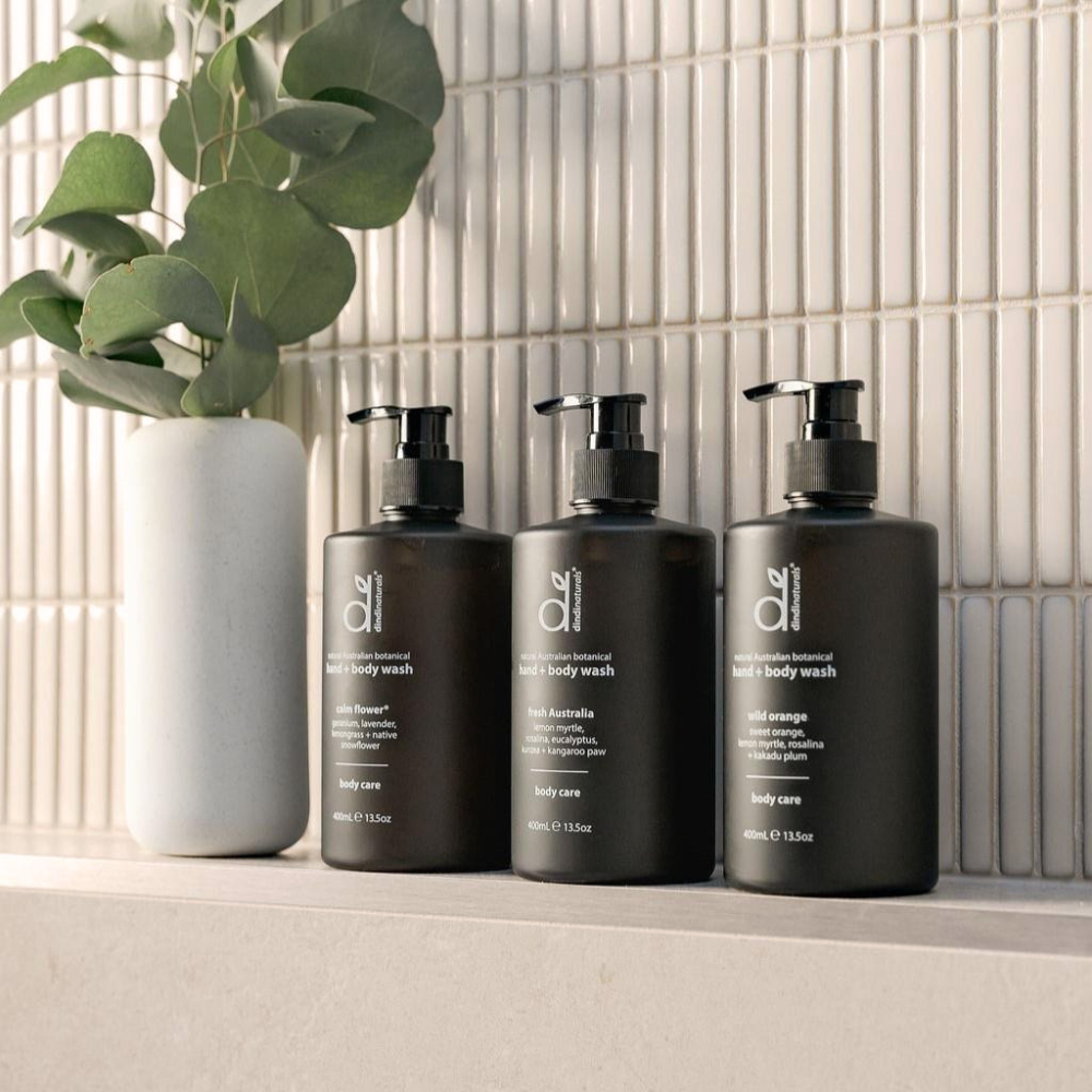 Three bottles of hand and body wash on a bathroom counter with a plant in the background.