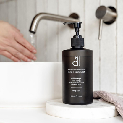 Black bottle of body wash on a bathroom counter with a hand washing in the background