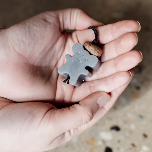 Hand holding a grey koala-shaped air freshener on a blurred background