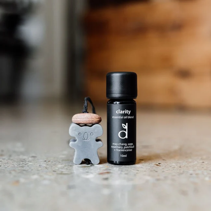 Small bottle of 'clarity' essential oil blend next to a koala-shaped air freshener on a concrete surface.