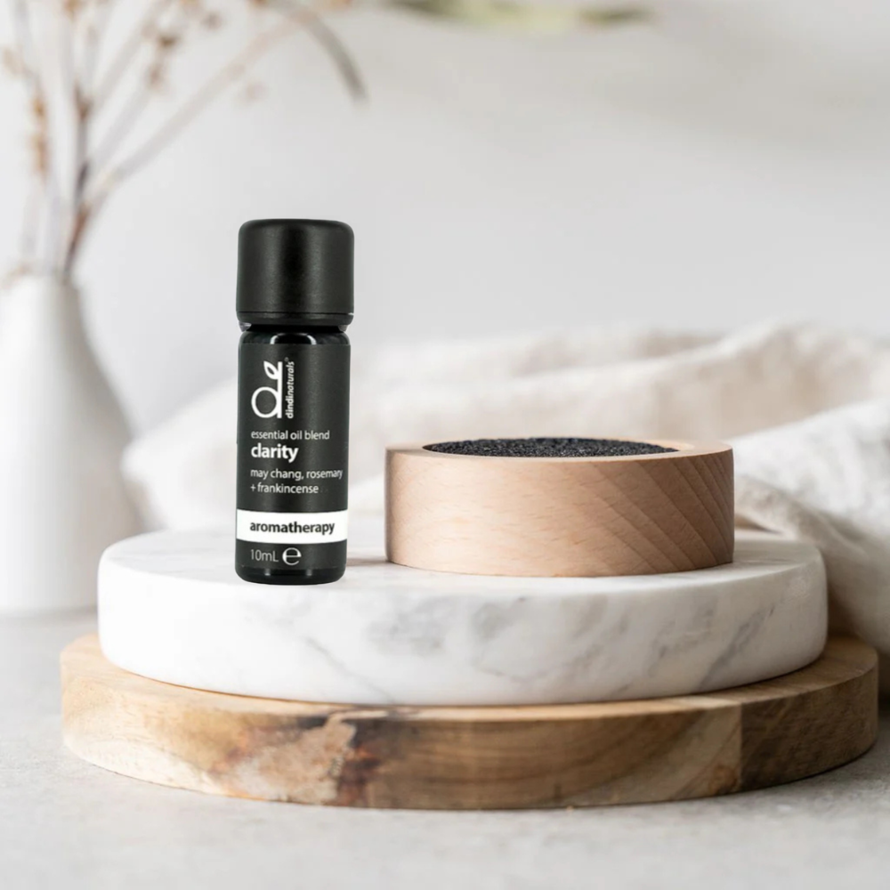 Lava rock diffuser and essential oil bottle labelled 'clarity' on a marble and wooden stand with a neutral background