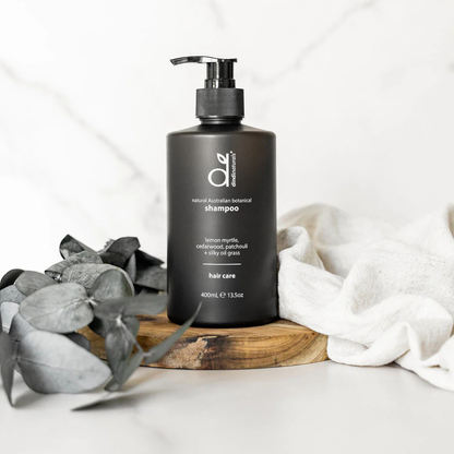 Black shampoo bottle styled on a wood stand with leaves