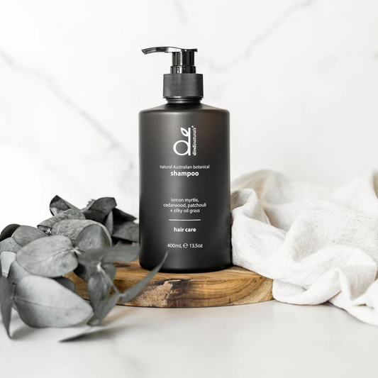 Black shampoo bottle styled on a wood stand with leaves