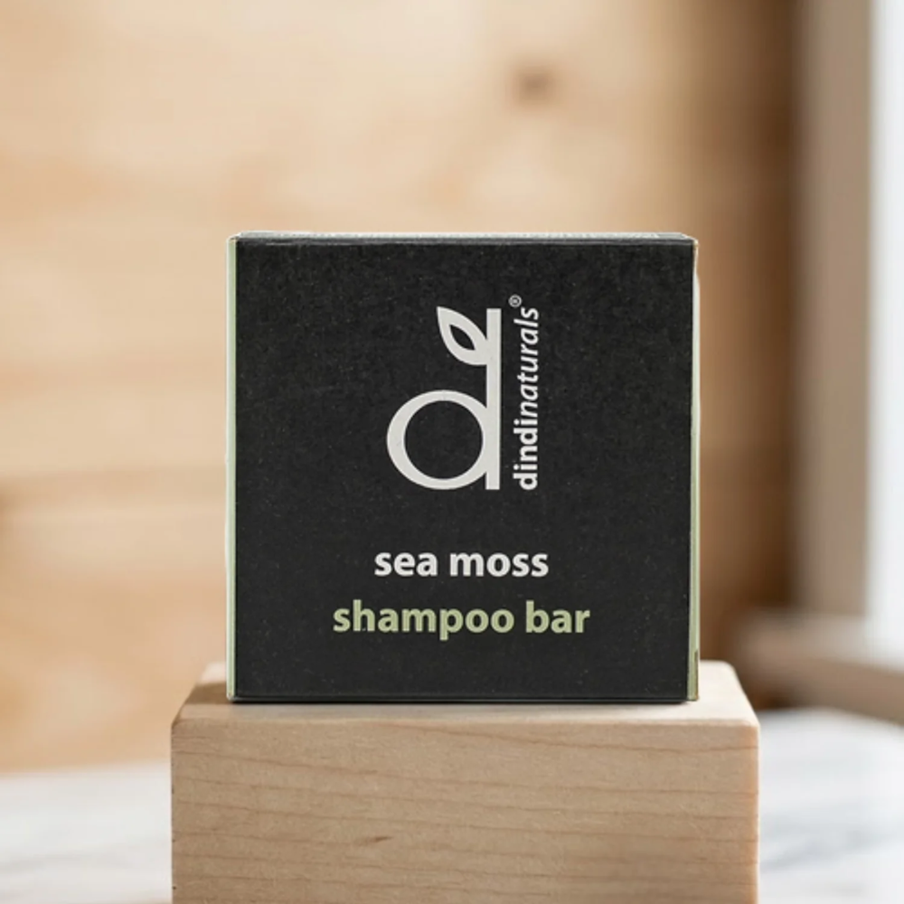Dindi Naturals sea moss shampoo bar packaging on a wooden block with a blurred background