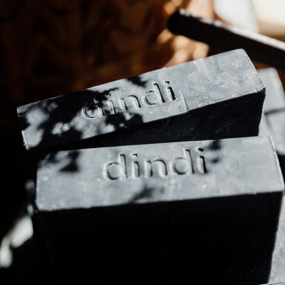 Two black bars of soap with 'dindi' branding on a blurred background