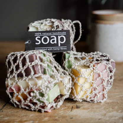 Handmade soap bars wrapped in hemp fibres with a tag -  '100% natural handmade soap' on a wooden surface.