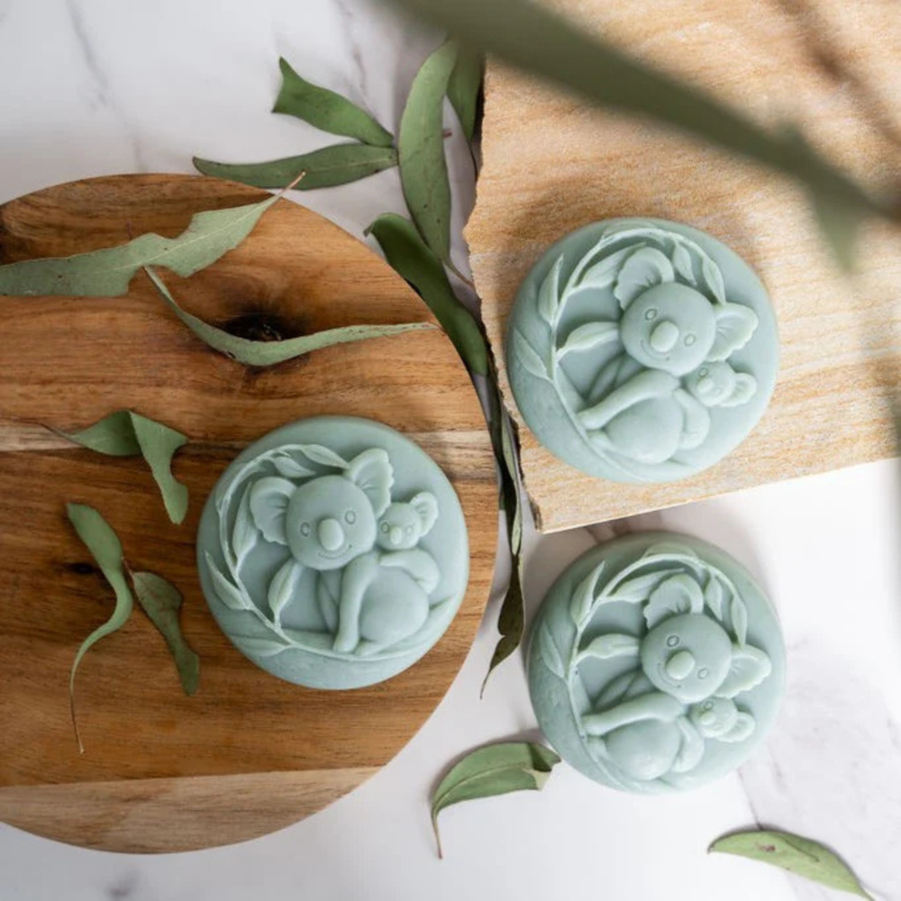 Green soap bars with koala designs on wood and stone boards with leaves.