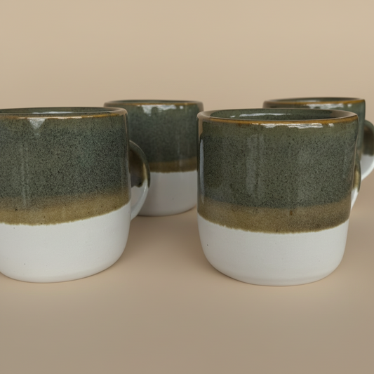 Four ceramic mugs with a green and white design on a beige background