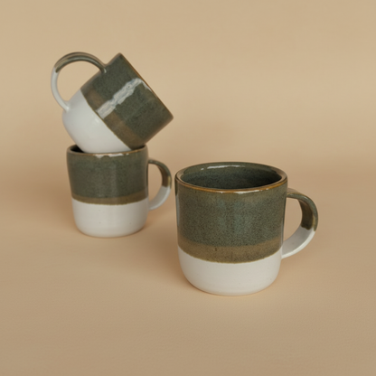 Three ceramic mugs with green and white glaze on a beige background