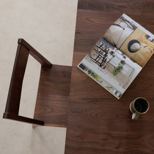 A Freya handcrafted ceramic mug is sitting next to an open book on a walnut dining table