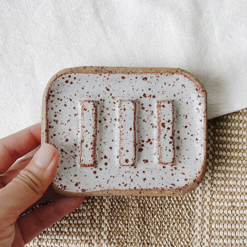 Hand holding a ceramic dish with a textured surface on a neutral background