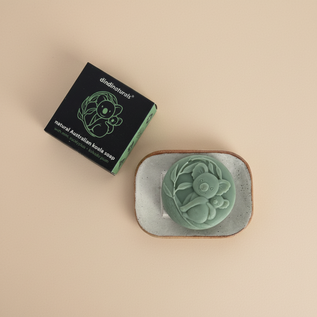 Green soap bar with koala design on a stone soap dish, next to its black packaging on a beige background.