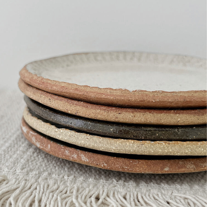 Stack of ceramic plates with textured surfaces on a textured fabric background