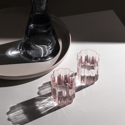 Two pink wave glasses filled with water next to a glass carafe