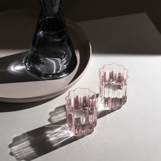 Two pink wave glasses filled with water next to a glass carafe