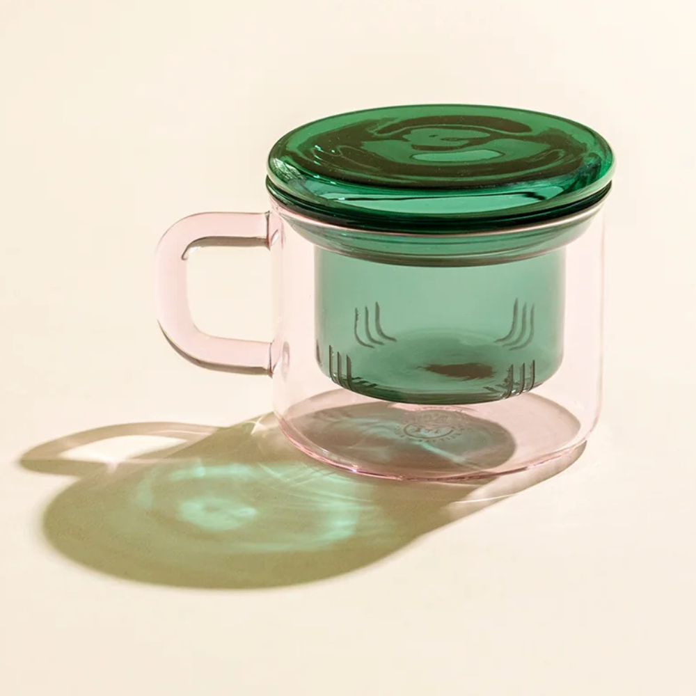 Pink glass mug with green lid on a beige background