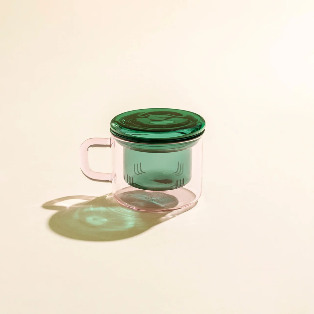 Pink glass mug with a green lid on a beige background