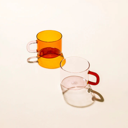 Two transparent glass mugs with coloured handles on a white background